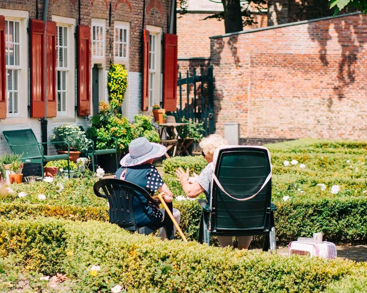 Zwei ältere Damen sitzen im Garten auf Gartenstühlen und unterhalten sich