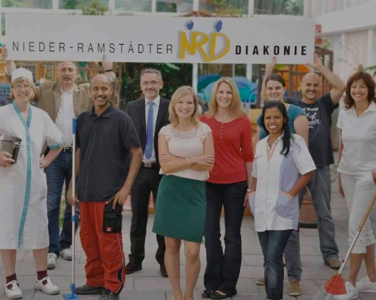 Mehrere Personen sind auf dem Bild zu sehen. Über ihnen ist ein Banner mit der Aufschrift "Nieder-Ramstädter NRD Diakonie"